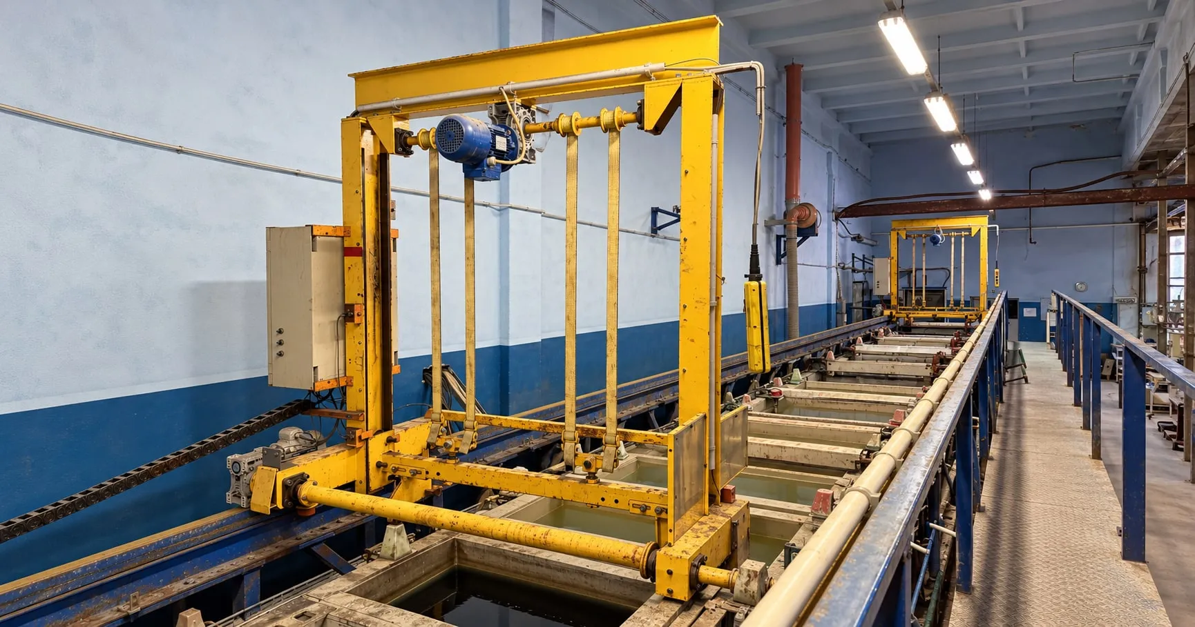Yellow gantry cranes above a galvanization tank line, with blue rails and a raised metal walkway
