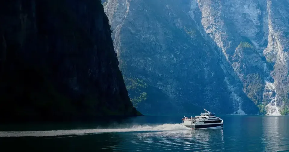 Passenger ferry crossing a calm fjord below steep rocky cliffs
